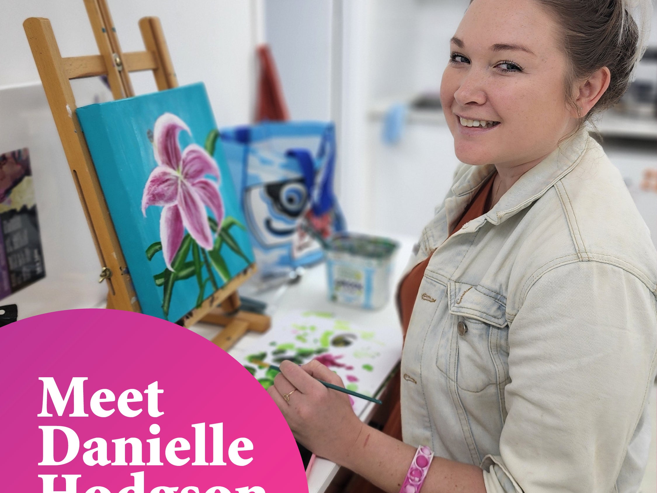 Young woman smiling at the camera whilst working on a painting of a flower with a bright blue background, next to the words "Meet Danielle Hodgson"