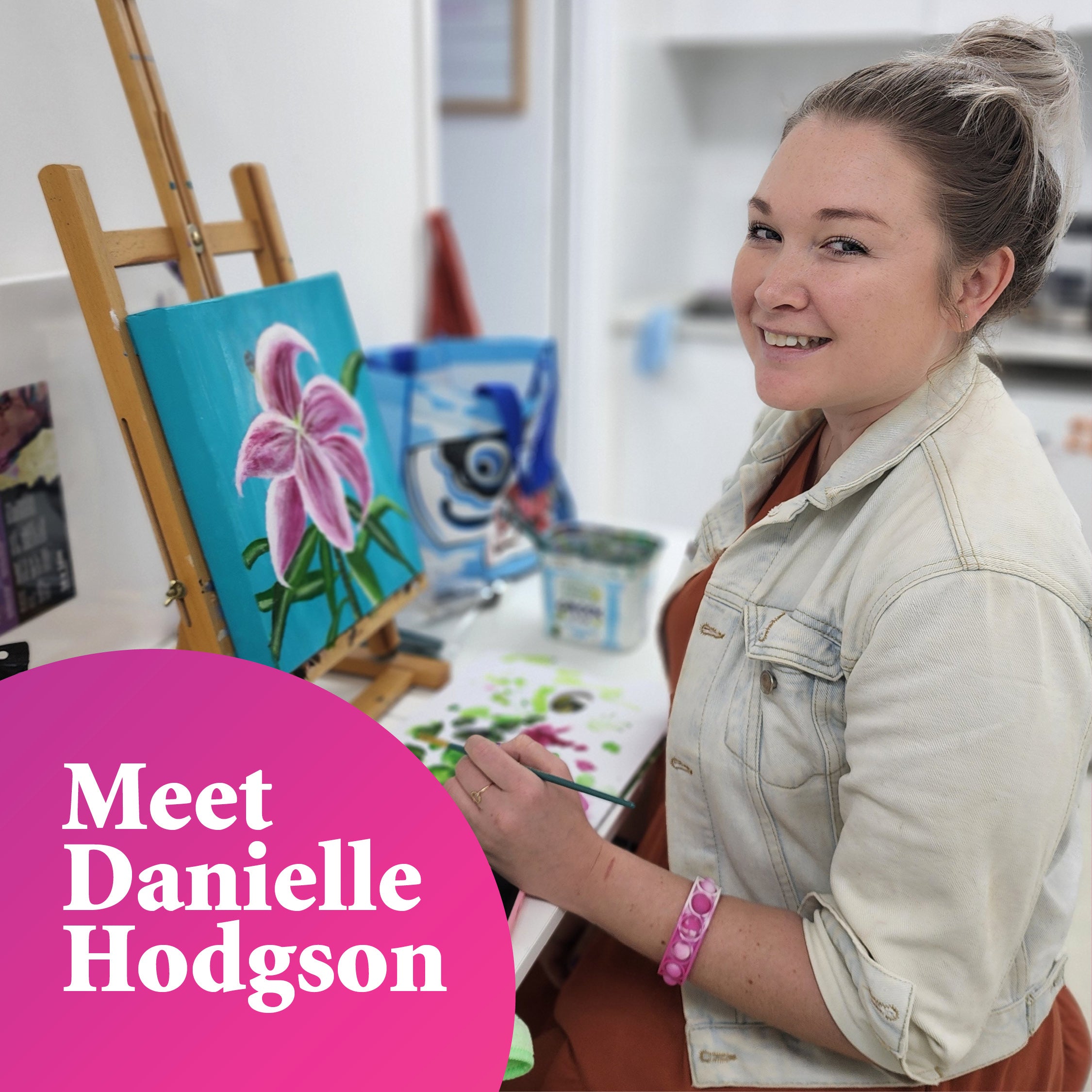 Young woman smiling at the camera whilst working on a painting of a flower with a bright blue background, next to the words "Meet Danielle Hodgson"