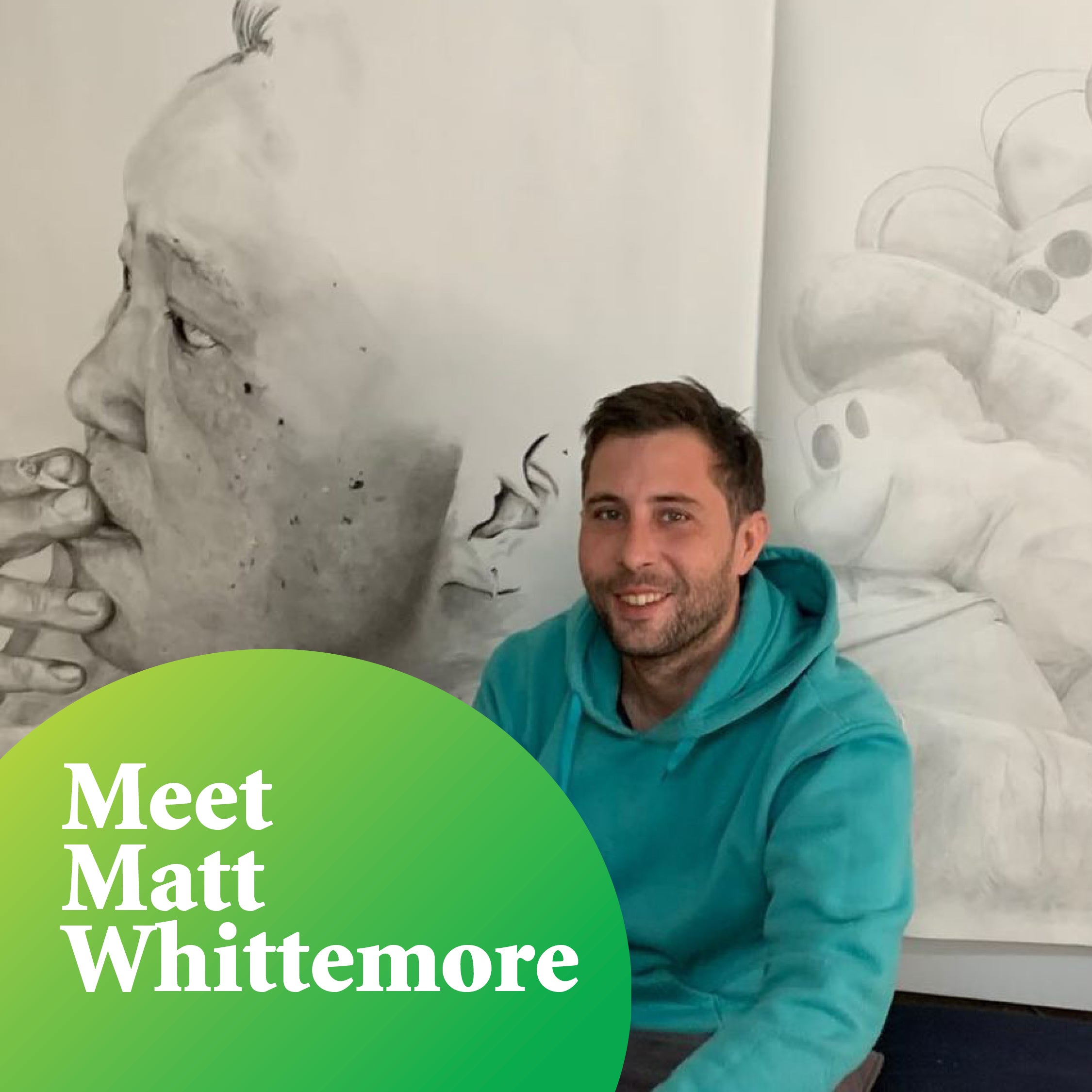 Pictured is Matt, smiling at the camera. He is wearing a teal hooded jumper and kneeling in front of two of his large, detailed, drawn artworks.  